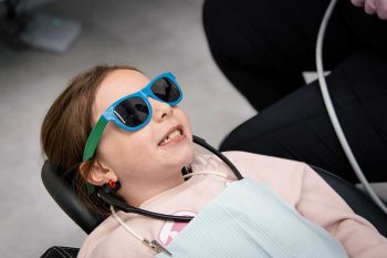 a young Millcreek Family Dental patient wearing sunglasses and smiling while laying in a dental chair
